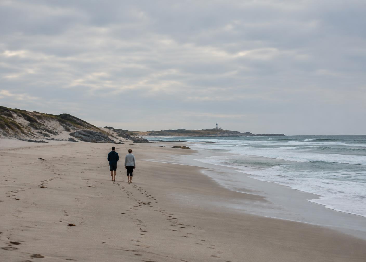 Two people walking a wide, empty Cape beach in soft light